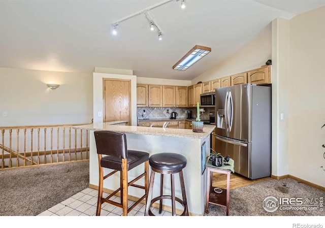 kitchen featuring vaulted ceiling, appliances with stainless steel finishes, light brown cabinets, and a kitchen bar