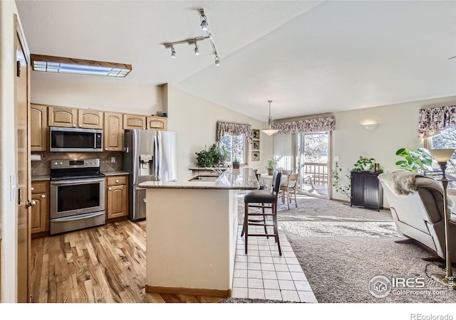 kitchen with vaulted ceiling, a kitchen island, appliances with stainless steel finishes, decorative light fixtures, and decorative backsplash