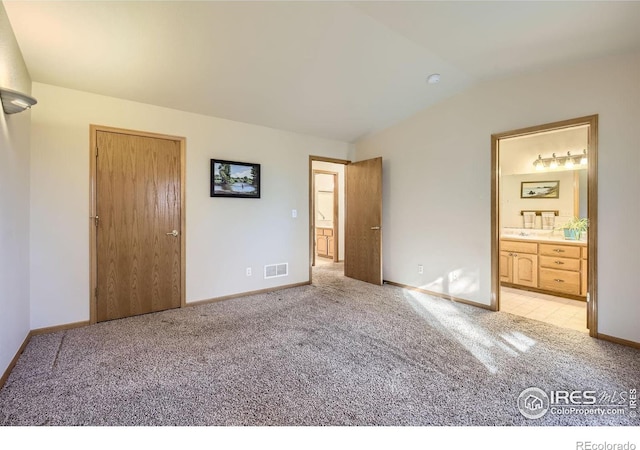 unfurnished bedroom with lofted ceiling, light carpet, and connected bathroom