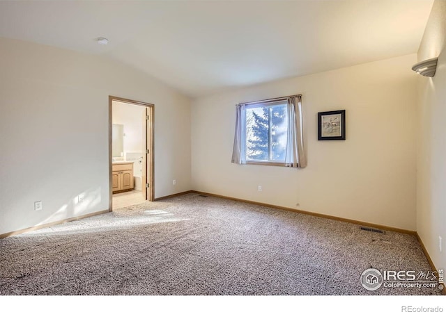 unfurnished bedroom with ensuite bathroom, vaulted ceiling, and light carpet