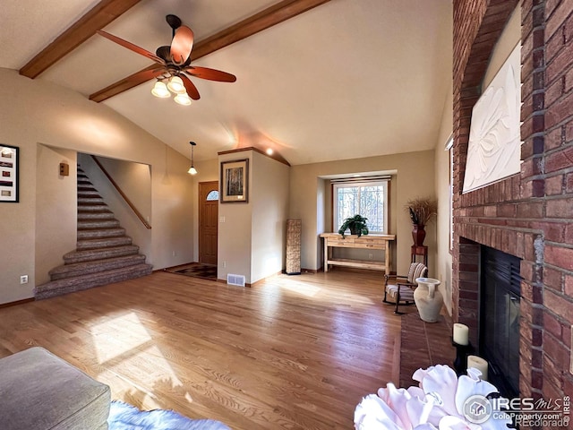 unfurnished living room featuring vaulted ceiling with beams, ceiling fan, wood-type flooring, and a brick fireplace