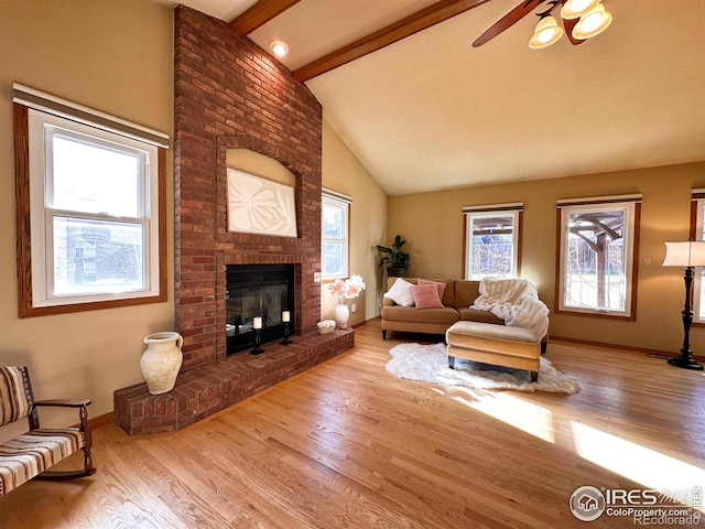 living room featuring ceiling fan, light hardwood / wood-style flooring, lofted ceiling with beams, and a brick fireplace