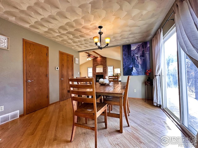 dining room with a brick fireplace, ceiling fan with notable chandelier, light hardwood / wood-style floors, and vaulted ceiling