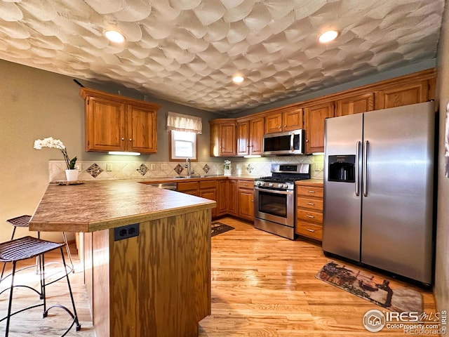 kitchen with kitchen peninsula, stainless steel appliances, light hardwood / wood-style flooring, and tasteful backsplash