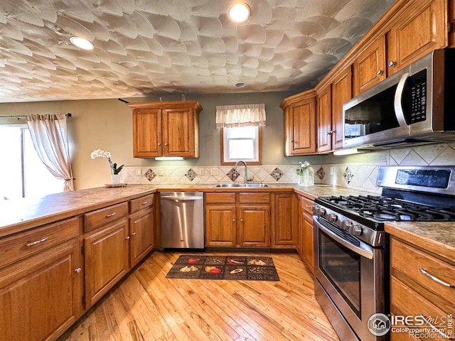 kitchen with sink, decorative backsplash, light wood-type flooring, appliances with stainless steel finishes, and kitchen peninsula