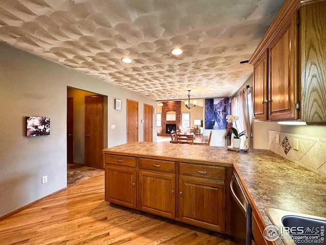 kitchen with tasteful backsplash, a textured ceiling, a large fireplace, dishwasher, and light hardwood / wood-style floors