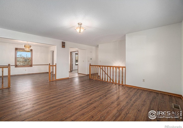 unfurnished room with dark hardwood / wood-style flooring, a chandelier, and a textured ceiling