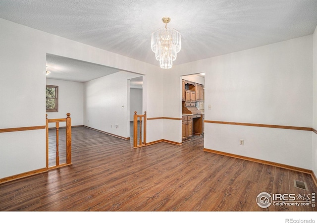 unfurnished room featuring a notable chandelier, dark hardwood / wood-style flooring, and a textured ceiling