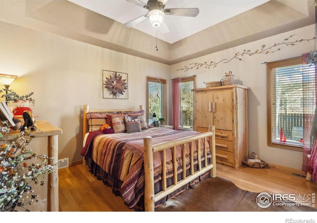 bedroom with hardwood / wood-style floors, ceiling fan, and a tray ceiling