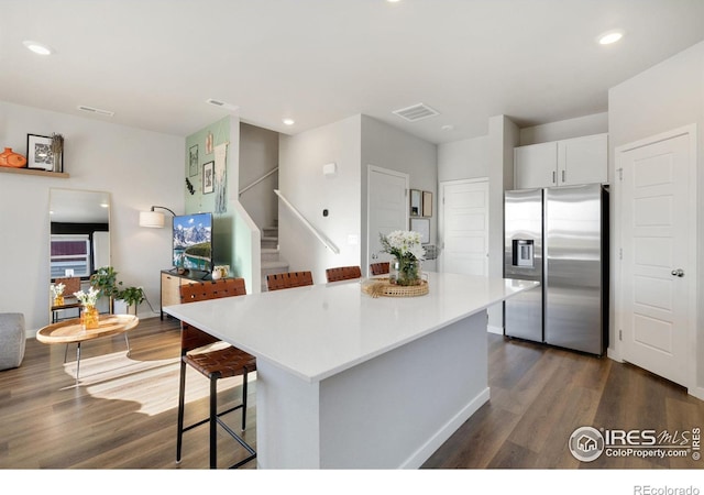 kitchen featuring white cabinetry, stainless steel refrigerator with ice dispenser, a center island, and a kitchen bar