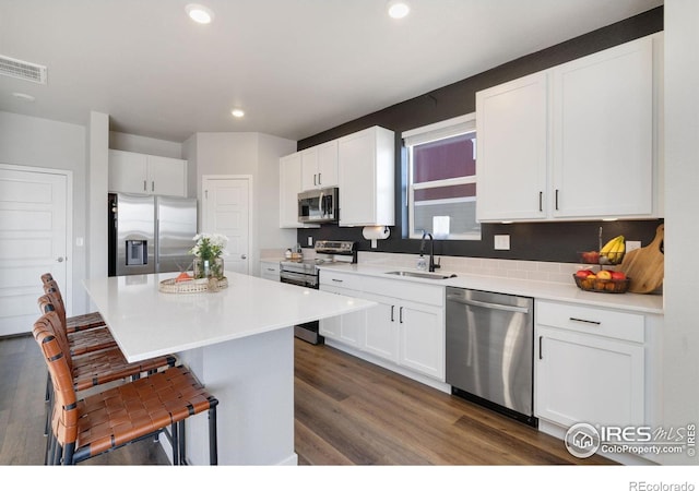 kitchen with a kitchen island, appliances with stainless steel finishes, white cabinetry, sink, and a kitchen bar