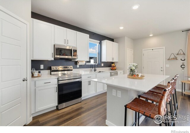 kitchen with sink, white cabinetry, stainless steel appliances, a kitchen island, and dark hardwood / wood-style flooring