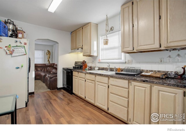 kitchen with sink, black range with electric stovetop, white refrigerator, light brown cabinetry, and light wood-type flooring