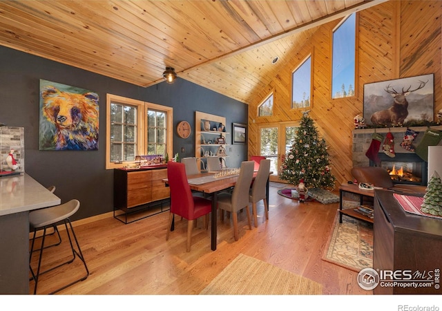 dining space with a fireplace, light hardwood / wood-style flooring, wooden ceiling, and wood walls