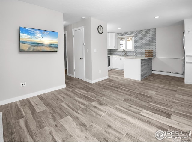 unfurnished living room featuring light wood-type flooring, a baseboard heating unit, and sink