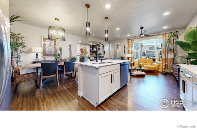 kitchen with dishwasher, dark wood-type flooring, hanging light fixtures, an island with sink, and white cabinetry