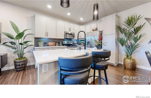 kitchen featuring decorative light fixtures, a breakfast bar, white cabinets, a center island with sink, and appliances with stainless steel finishes