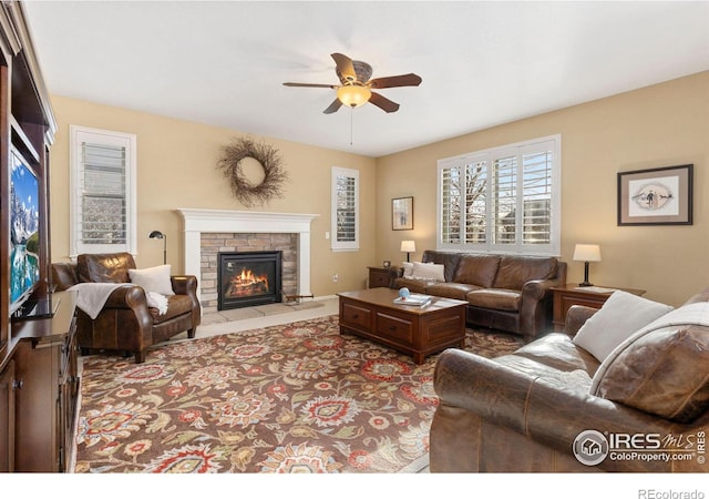 living room featuring a stone fireplace and ceiling fan