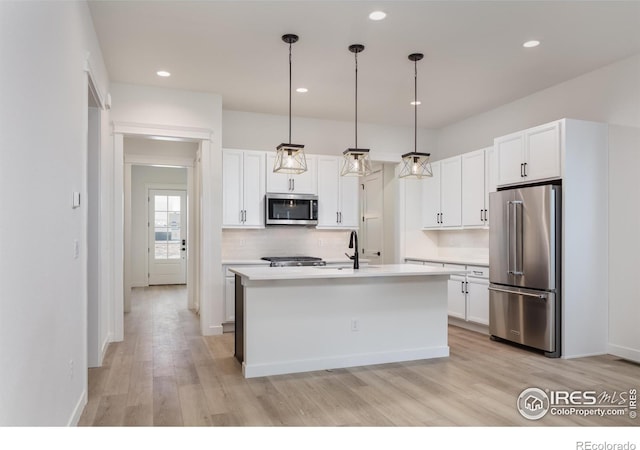 kitchen with white cabinetry, appliances with stainless steel finishes, a kitchen island with sink, and hanging light fixtures