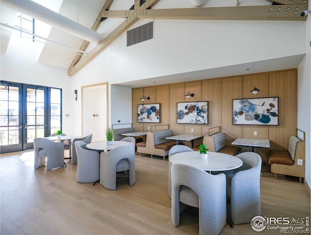 interior space featuring french doors, light wood-type flooring, beamed ceiling, wood walls, and high vaulted ceiling