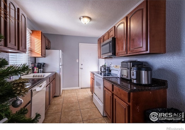 kitchen with dark stone counters, a textured ceiling, white appliances, sink, and light tile patterned floors