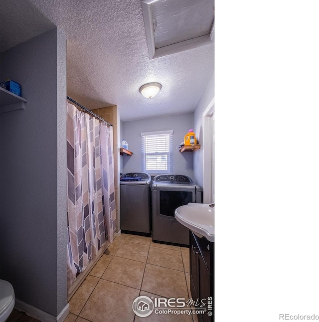 laundry room featuring a textured ceiling, washing machine and dryer, and light tile patterned floors