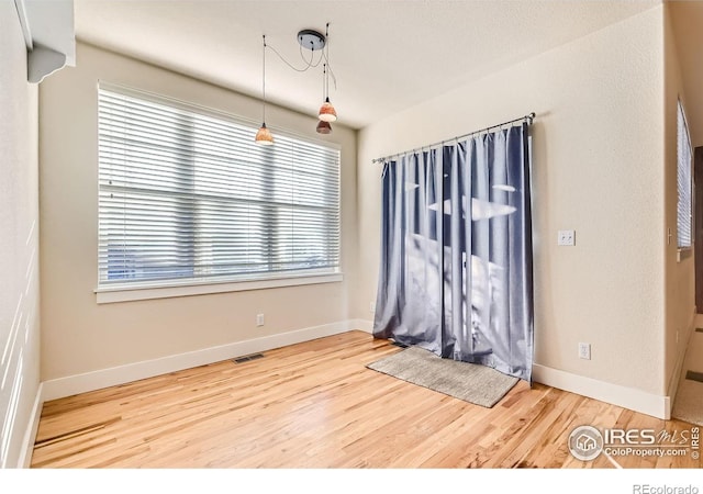 empty room featuring wood finished floors, visible vents, and baseboards