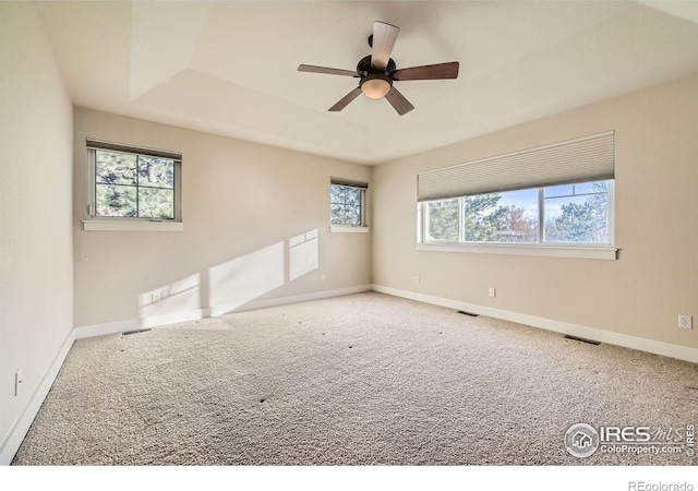 carpeted spare room featuring visible vents, a raised ceiling, and baseboards