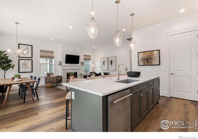 kitchen with a center island with sink, sink, pendant lighting, dishwasher, and light stone countertops