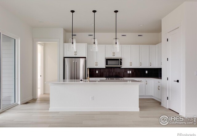 kitchen featuring a center island with sink, hanging light fixtures, stainless steel appliances, light countertops, and white cabinetry