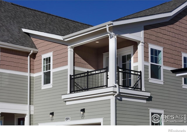 view of side of home featuring roof with shingles and a balcony