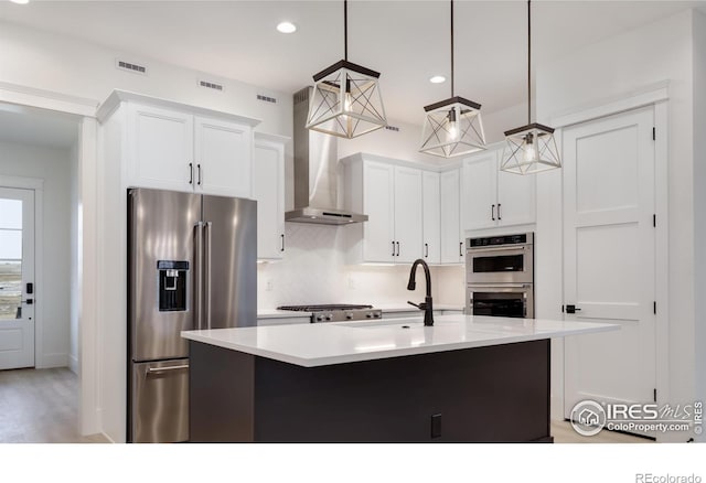 kitchen with white cabinets, stainless steel appliances, wall chimney exhaust hood, and decorative light fixtures