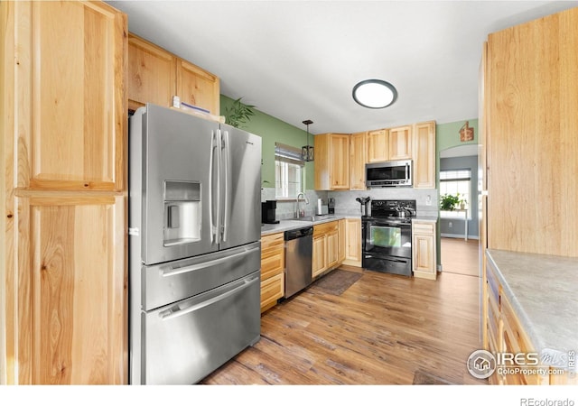 kitchen featuring appliances with stainless steel finishes, light brown cabinets, hanging light fixtures, and sink