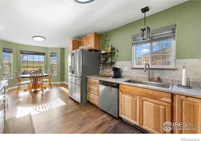 kitchen featuring appliances with stainless steel finishes, backsplash, sink, wood-type flooring, and hanging light fixtures