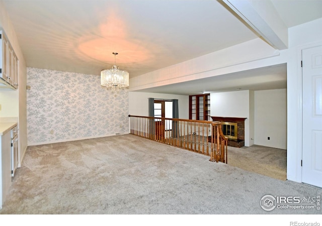 spare room featuring light carpet, a fireplace, beamed ceiling, and an inviting chandelier