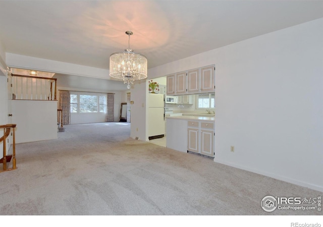 interior space featuring pendant lighting, white appliances, sink, light colored carpet, and a chandelier