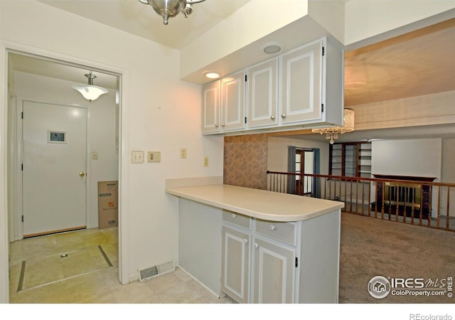 kitchen featuring kitchen peninsula, white cabinetry, light carpet, and a chandelier