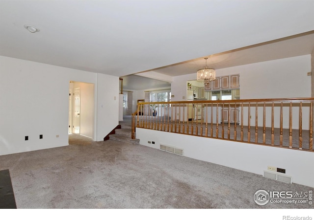 carpeted empty room with an inviting chandelier