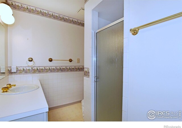 bathroom with vanity, a shower with door, and tile walls