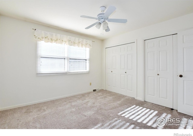 unfurnished bedroom with ceiling fan, light carpet, and two closets