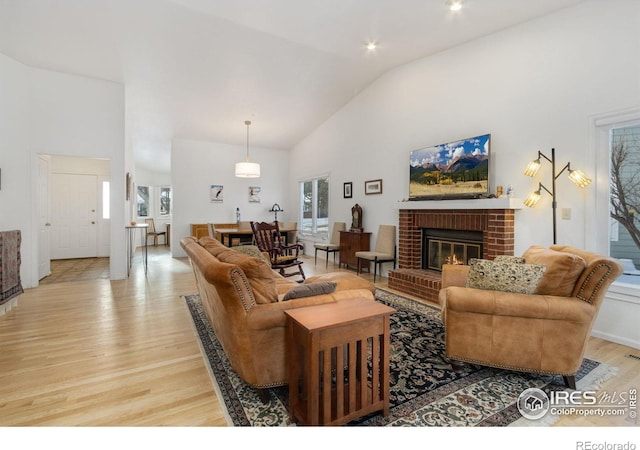 living room featuring a brick fireplace, high vaulted ceiling, and light hardwood / wood-style floors