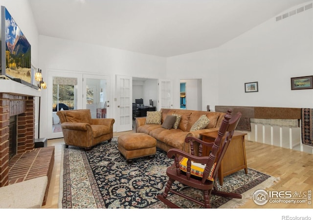 living room featuring a brick fireplace, light hardwood / wood-style flooring, and french doors