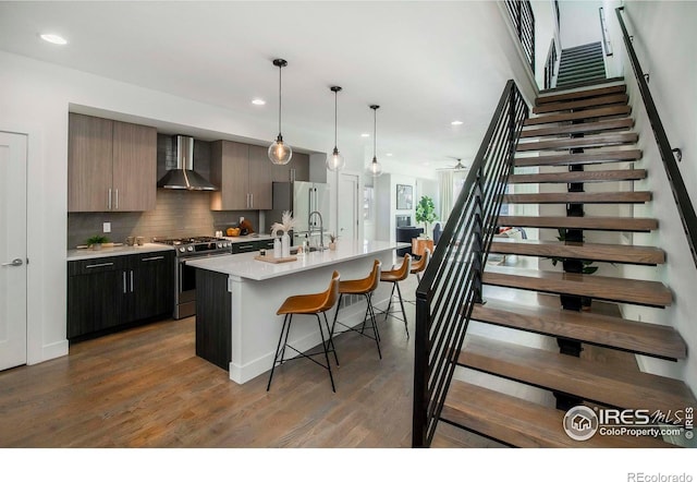 kitchen with a center island with sink, wall chimney exhaust hood, hardwood / wood-style floors, and appliances with stainless steel finishes