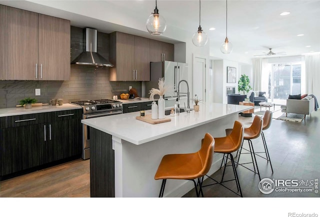 kitchen with a center island with sink, wall chimney range hood, and high end appliances