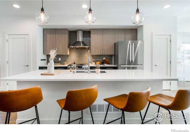 kitchen with a center island with sink, decorative backsplash, stainless steel fridge, and wall chimney range hood