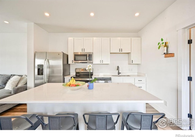 kitchen featuring sink, a kitchen breakfast bar, a center island with sink, white cabinets, and appliances with stainless steel finishes