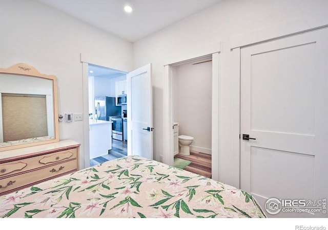 bedroom featuring hardwood / wood-style floors, stainless steel fridge with ice dispenser, and ensuite bath