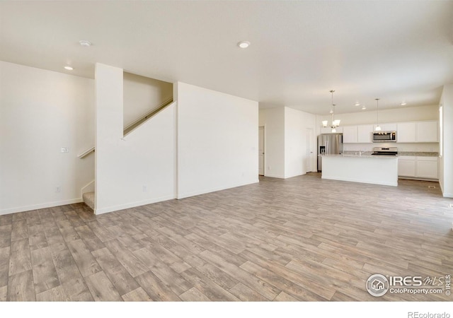 unfurnished living room with a chandelier and light wood-type flooring