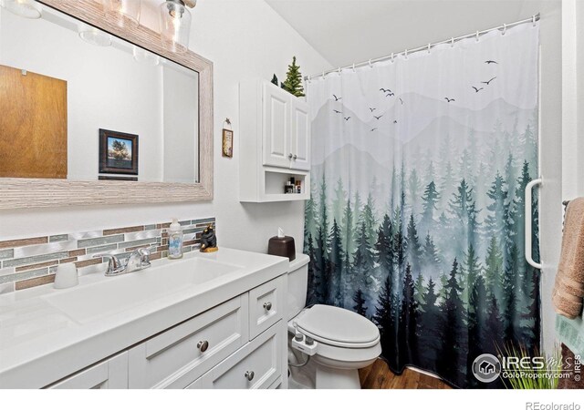 bathroom featuring vanity, backsplash, hardwood / wood-style flooring, toilet, and curtained shower