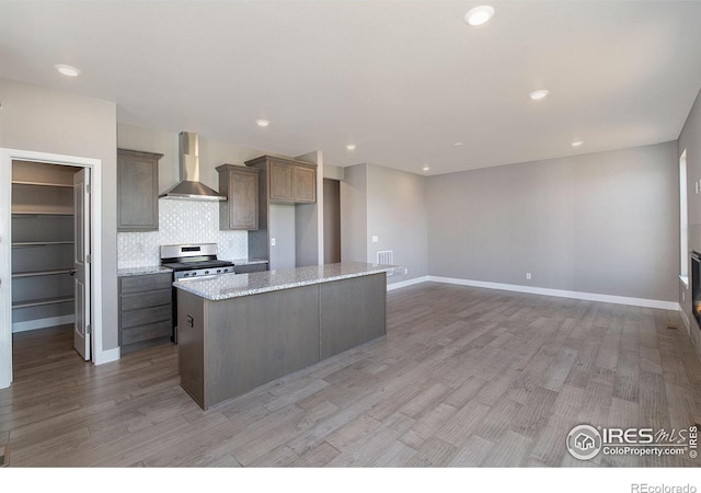 kitchen featuring a center island, wall chimney range hood, light stone countertops, light hardwood / wood-style floors, and stainless steel range oven